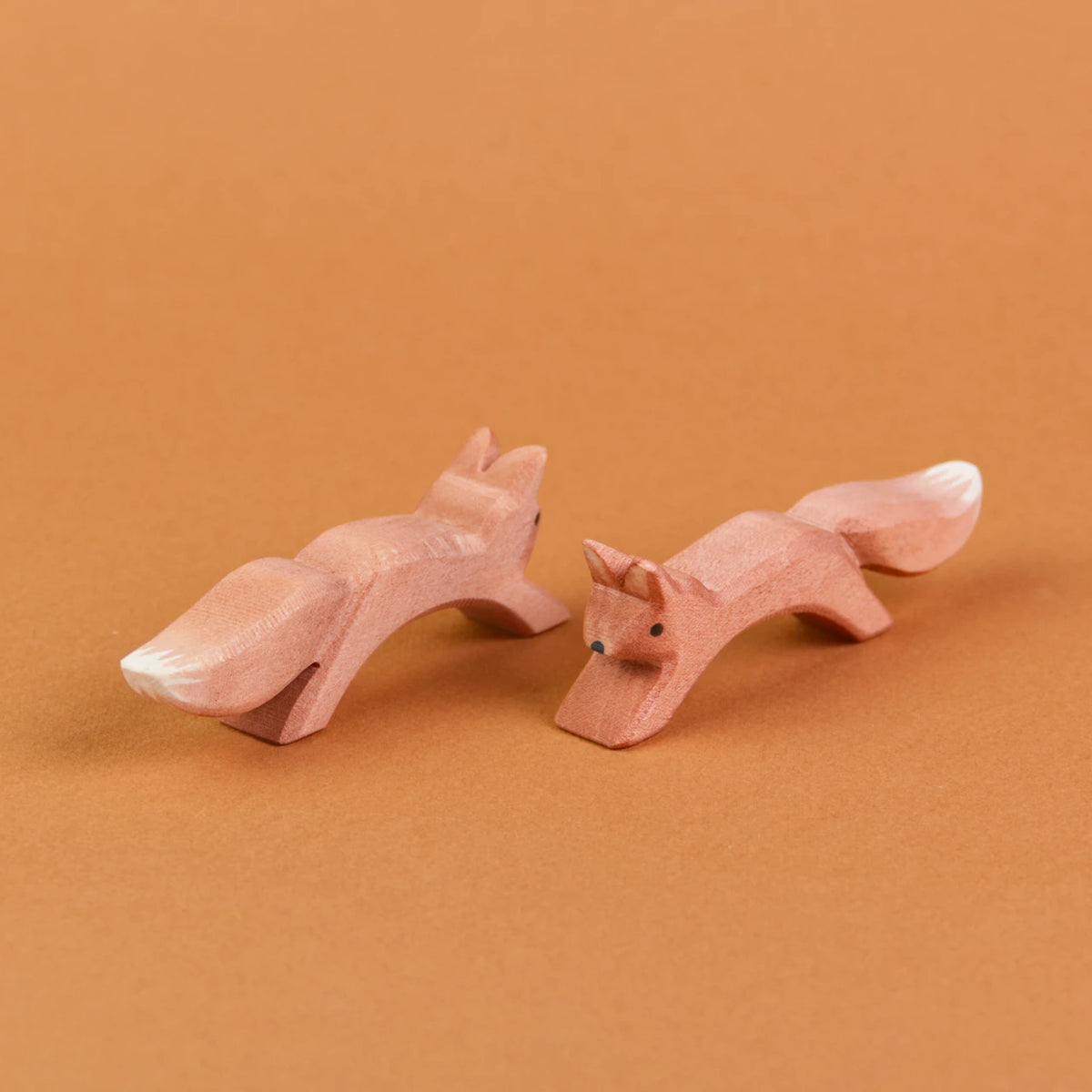 Es sind zwei springende Eichhörnchen aus Holz zu sehen, die parallel, nebeneinander stehen. Das linke Eichhörnchen schaut nach hinten rechts, das rechte Eichhörnchen schaut nach vorne links.