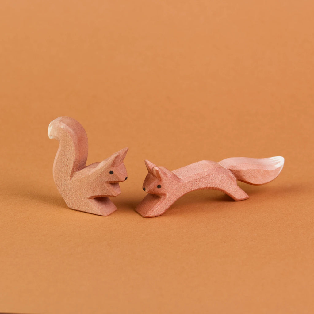 Es sind zwei Eichhörnchen aus Holz sich gegenüber sitzend zu sehen. Ein springendes Eichhörnchen ist rechts zu sehen und schaut nach vorne links. Links davon ist ein sitzendes Eichhörnchen zu sehen, das zu dem anderen nach rechts rüber schaut.