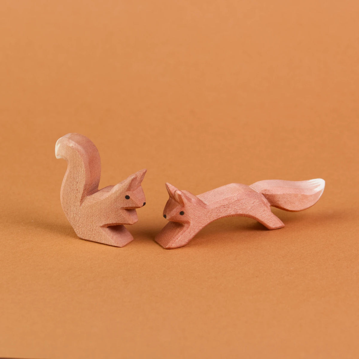 Es sind zwei Eichhörnchen aus Holz sich gegenüber sitzend zu sehen. Ein springendes Eichhörnchen ist rechts zu sehen und schaut nach vorne links. Links davon ist ein sitzendes Eichhörnchen zu sehen, das zu dem anderen nach rechts rüber schaut.