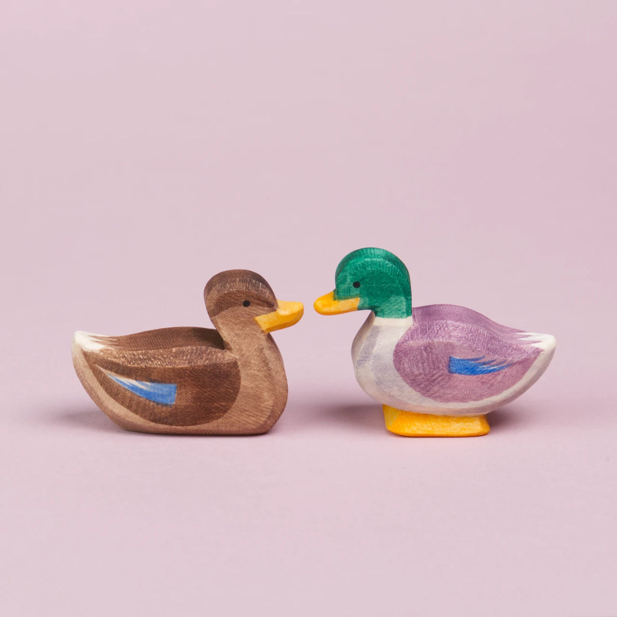 Ein Erpel rechts und eine Ente links aus Holz sitzen sich gegenüber und sind in der Seitenansicht zu sehen. Sie schauen sich an und berühren sich fast mit ihrem gelben Schnabel.