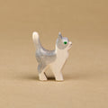 Eine kleine Katze aus Holz von der Marke Ostheimer ist von der Seitenansicht zu sehen und hält ihren Kopf, sowie auch den Schwanz nach oben. Der Großteil ihres Felles ist weiß gefärbt und der obere Part des Kopfes mit den Ohren, sowie der Rücken über einen Teil der Hinterbeine bis zu den Schwanz ist dunkelgrau eingefärbt. Die Augen der kleinen Katze sind dunkelgrün.