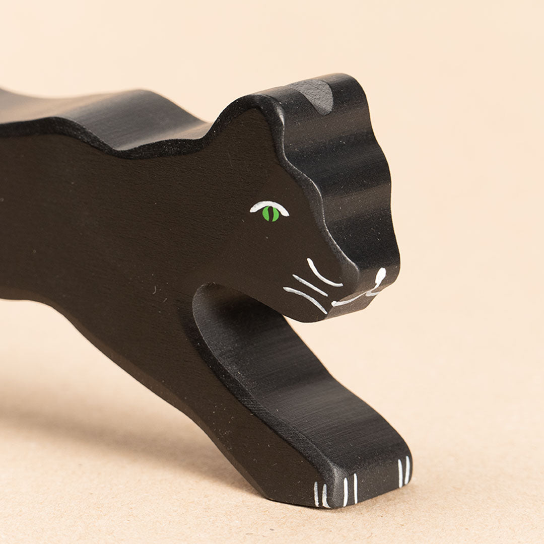 Die Nahaufnahme zeigt einen schwarzen Panther aus Holz. Seine Augen sind hellgrün aufgemalt. Die Pfoten, sowie Nase und Barthaare werden durch weiße Bemalung erkenntlich. Sein Blick richtet sich nach vorne rechts. Sein Körper ist bis zur Körpermitte hin sichtbar.