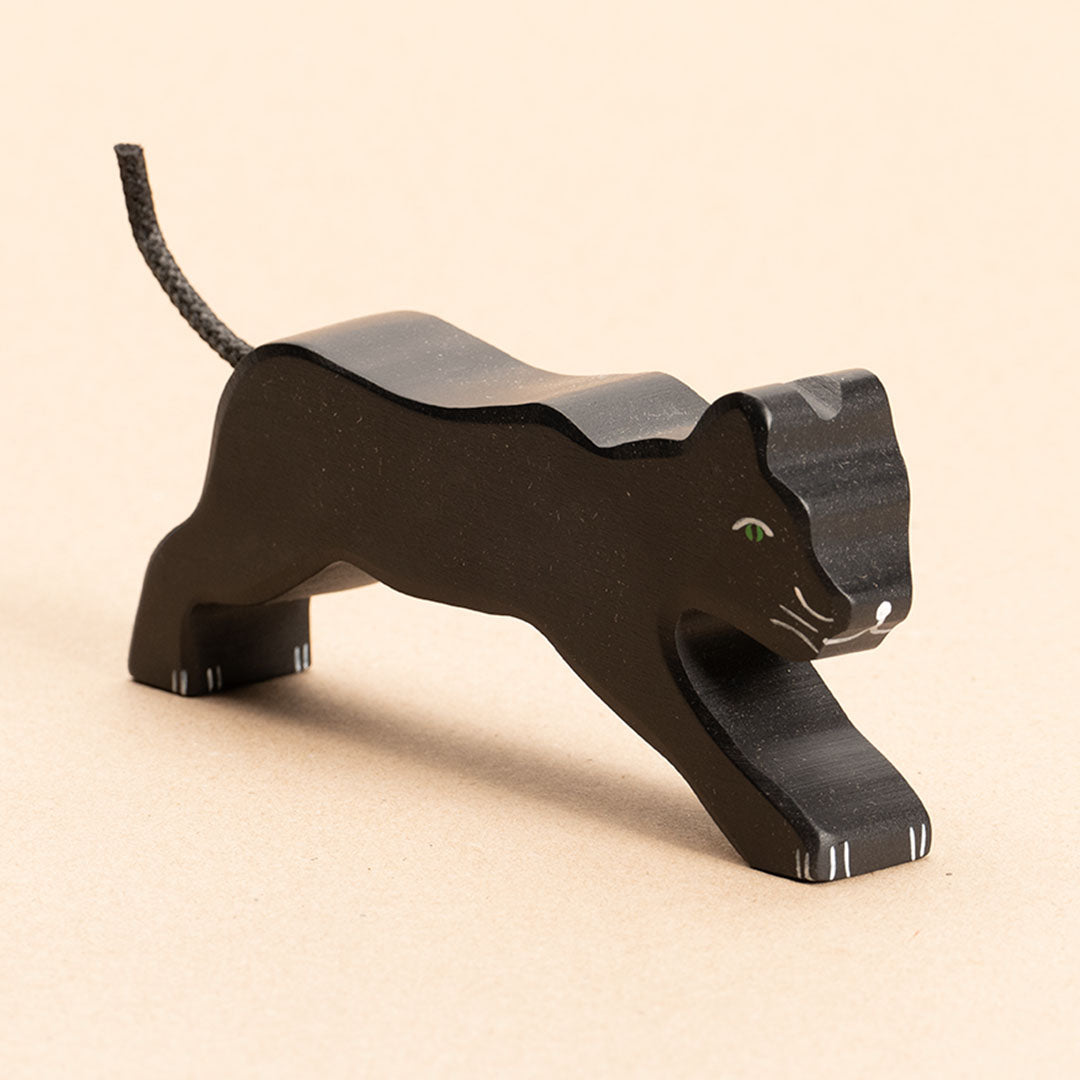 Ein nach vorne rechts schauender Panther aus Naturholz, ist komplett schwarz, hat einen schwarzen, weit nach oben hin stehenden Schwanz aus Kordel, hellgrüne Augen, sowie weiße Bemalung für Pfoten und Baarthaare und Nase. Beide Beinpaare hat er weit auseinander gespreizt.