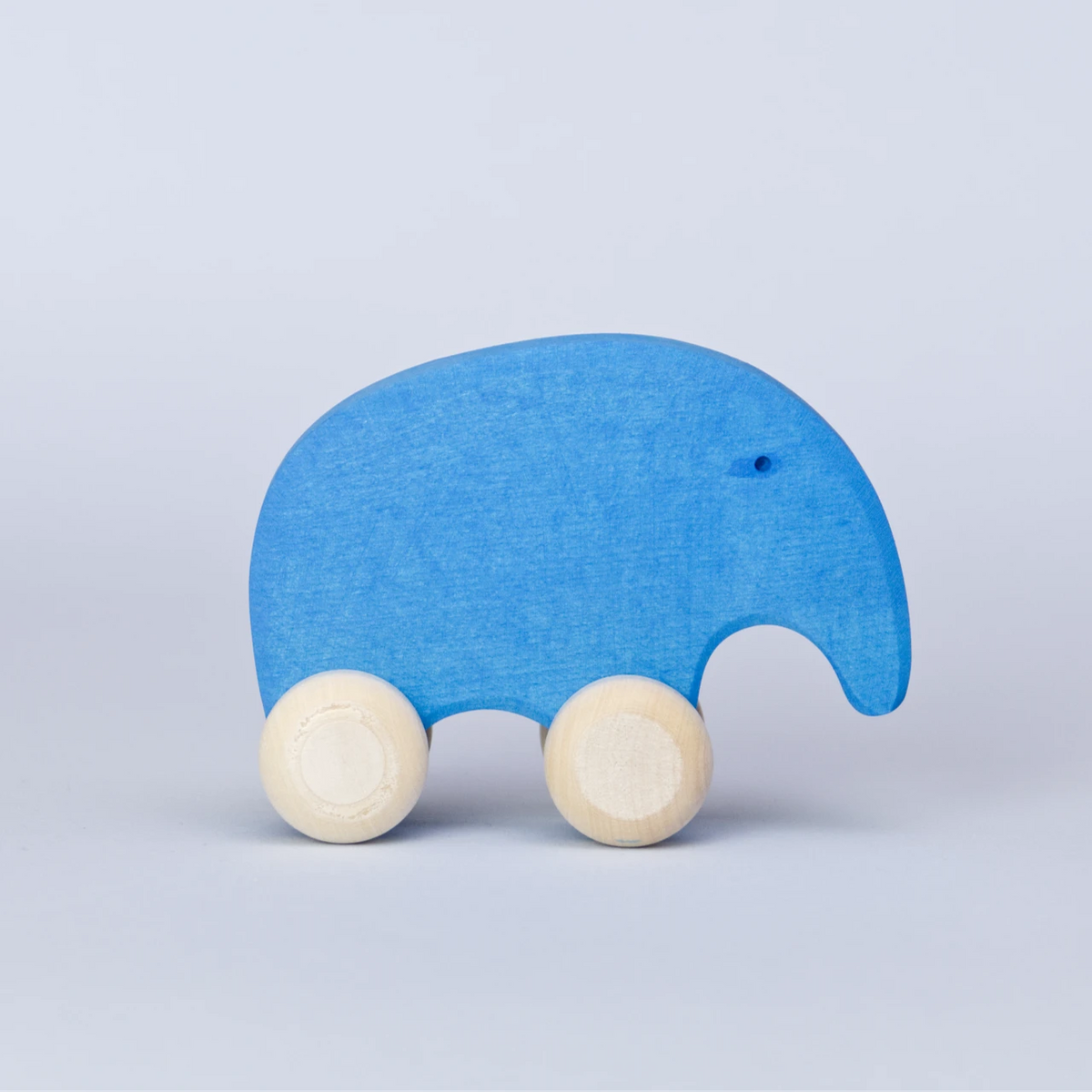 Ein blaues Schiebetier mit weißen Rädern von Goki Evolution ist in der Seitenansicht zu sehen. Die Form erinnert abstrahiert an einen Elefanten, dieser schaut nach rechts. Sein Auge ist ein kleines Loch. Es ist aus Holz gefertigt. Seine Farbe ist ein Azurblau.
