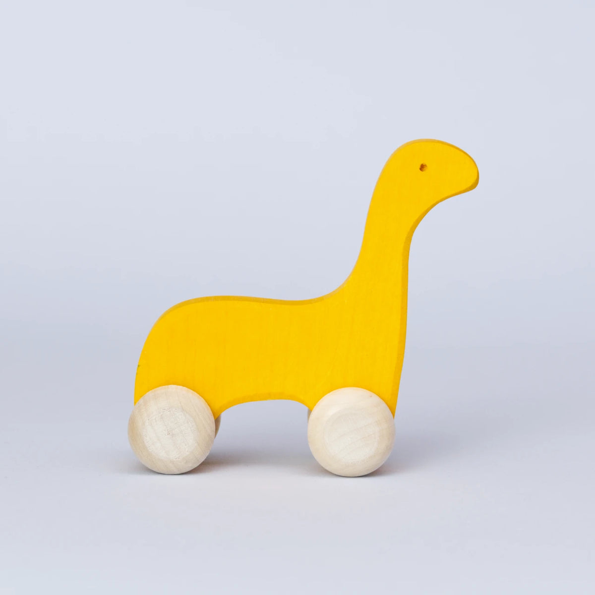 Ein gelbes Schiebetier mit weißen Rädern von Goki Evolution ist in der Seitenansicht zu sehen. Die Form erinnert an einen Dinosaurier mit langem Hals oder einer Giraffe. Das Tier schaut nach rechts mit einem kleinen Auge, dieses wird durch ein gebohrtes Loch angedeutet. Es ist aus Holz gefertigt und die Farbe ist ein intensives, freundliches Sonnengelb.