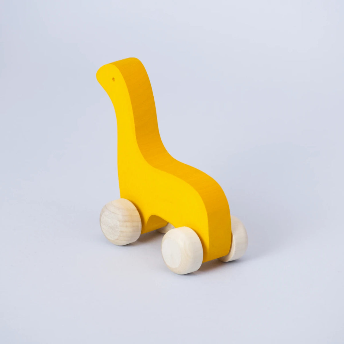 Ein gelbes Schiebetier mit weißen Rädern von Goki Evolution ist schräg von hinten zu sehen. Die Form erinnert an einen Dinosaurier mit langem Hals oder einer Giraffe. Das Tier schaut nach hinten links. Es ist aus Holz gefertigt und die Farbe ist ein intensives, freundliches Sonnenblumen Gelb.