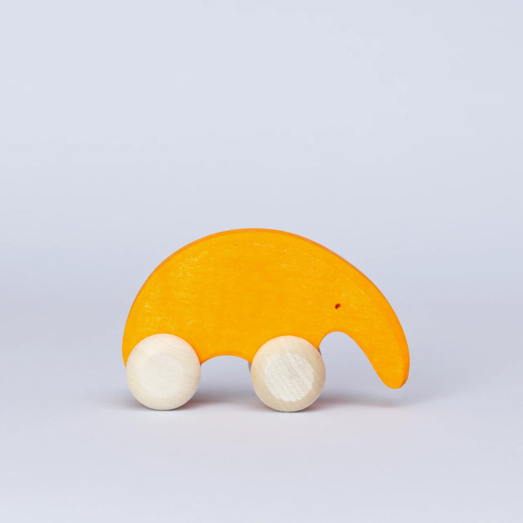 Ein orangenes Schiebetier mit weißen Rädern von Goki Evolution ist in der Seitenansicht zu sehen. Die Form erinnert an einen Ameisenbär mit seiner langen Schnauze. Das Tier schaut nach rechts mit einem kleinen Loch als Auge. Es ist aus Holz gefertigt und die Farbe ist ein warmes Orange.