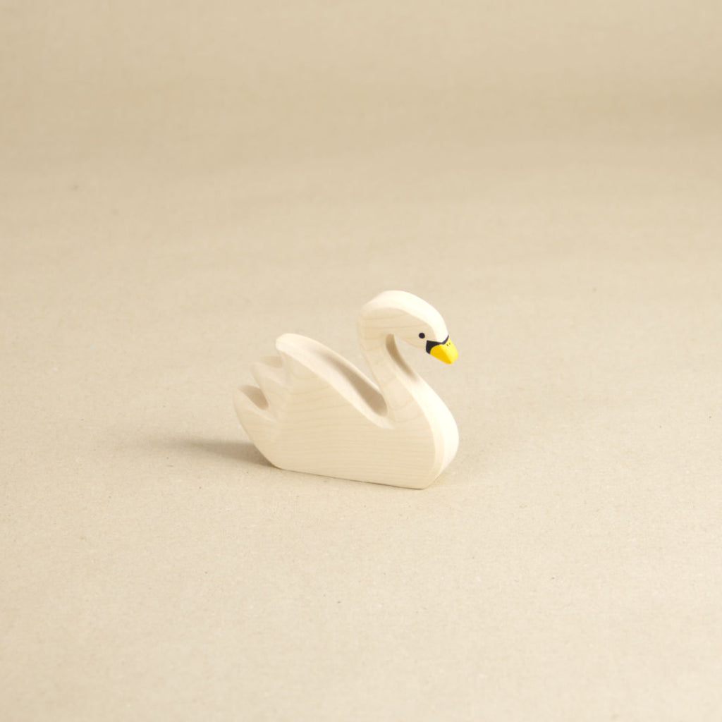 Ein schwimmender Schwan aus Naturholz gefertigt, schaut nach vorne rechts. Er hat einen gelben Schnabel mit schwarzen Farbdetails, sowie nach hinten, oben abstehenden Gefieder.