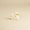 Ein schwimmender Schwan aus Naturholz gefertigt, schaut nach vorne rechts. Er hat einen gelben Schnabel mit schwarzen Farbdetails, sowie nach hinten, oben abstehenden Gefieder.