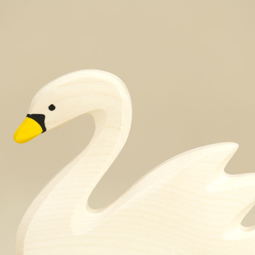 Eine Nahaufnahme eines schwimmenden Schwans aus Naturholz von Holztiger gefertigt, ist im Profil fotografiert und schaut nach links. Er hat einen gelben Schnabel mit schwarzen Farbdetails. Ein Teil seines nach hinten oben abstehenden Gefieders ist nicht mehr ganz zu sehen.