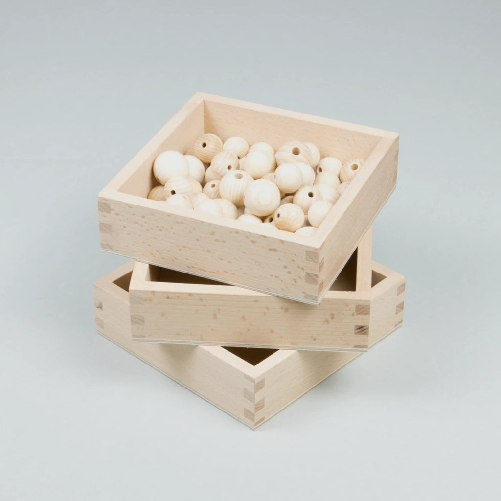 Gestapelte Holzkisten, wovon die obere mit Holzkugeln gefüllt ist.