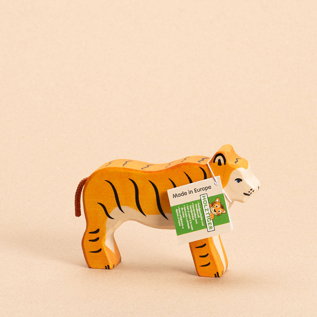 Ein nach rechts schauender Tiger im Profil von Holztiger aus Ahorn- und Buchenholz gefertigt, hat orangenes Fell mit schwarzen, senkrechten Streifen. Das Gesicht und Bauchfell sind weiß. Sein orangener Schwanz aus Kordel ist nach unten hin geneigt.