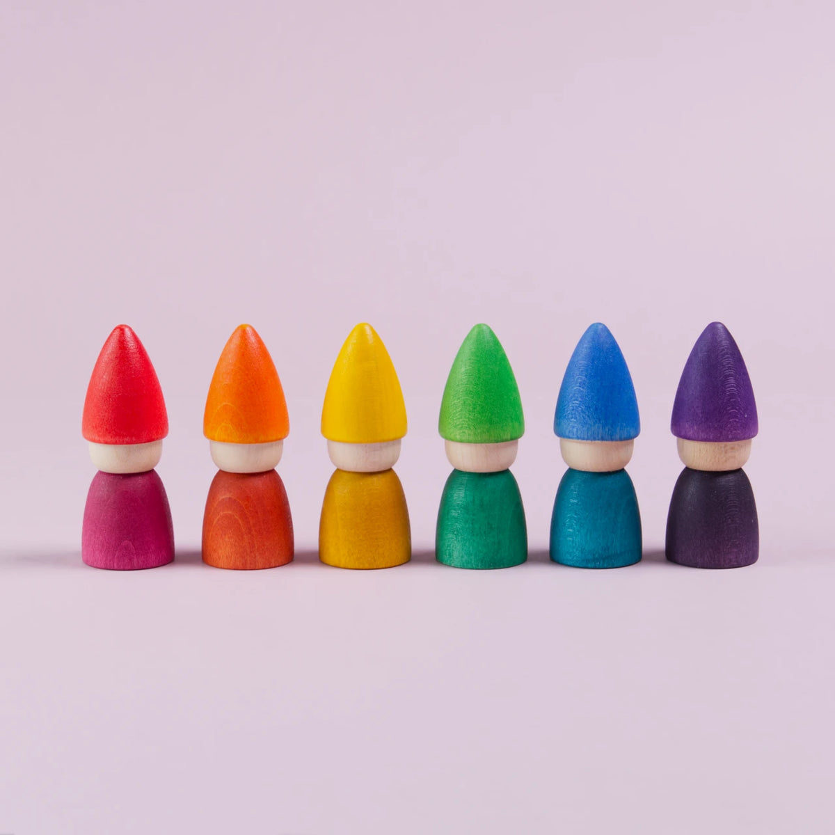 Mittig im Bild nebeneinander aufgereihte Figuren mit einer spitzen Mütze und mit farblich gleichem Oberkörper. In rot. orange, gelb, grün, blau und lila. Alle haben kein Gesicht.