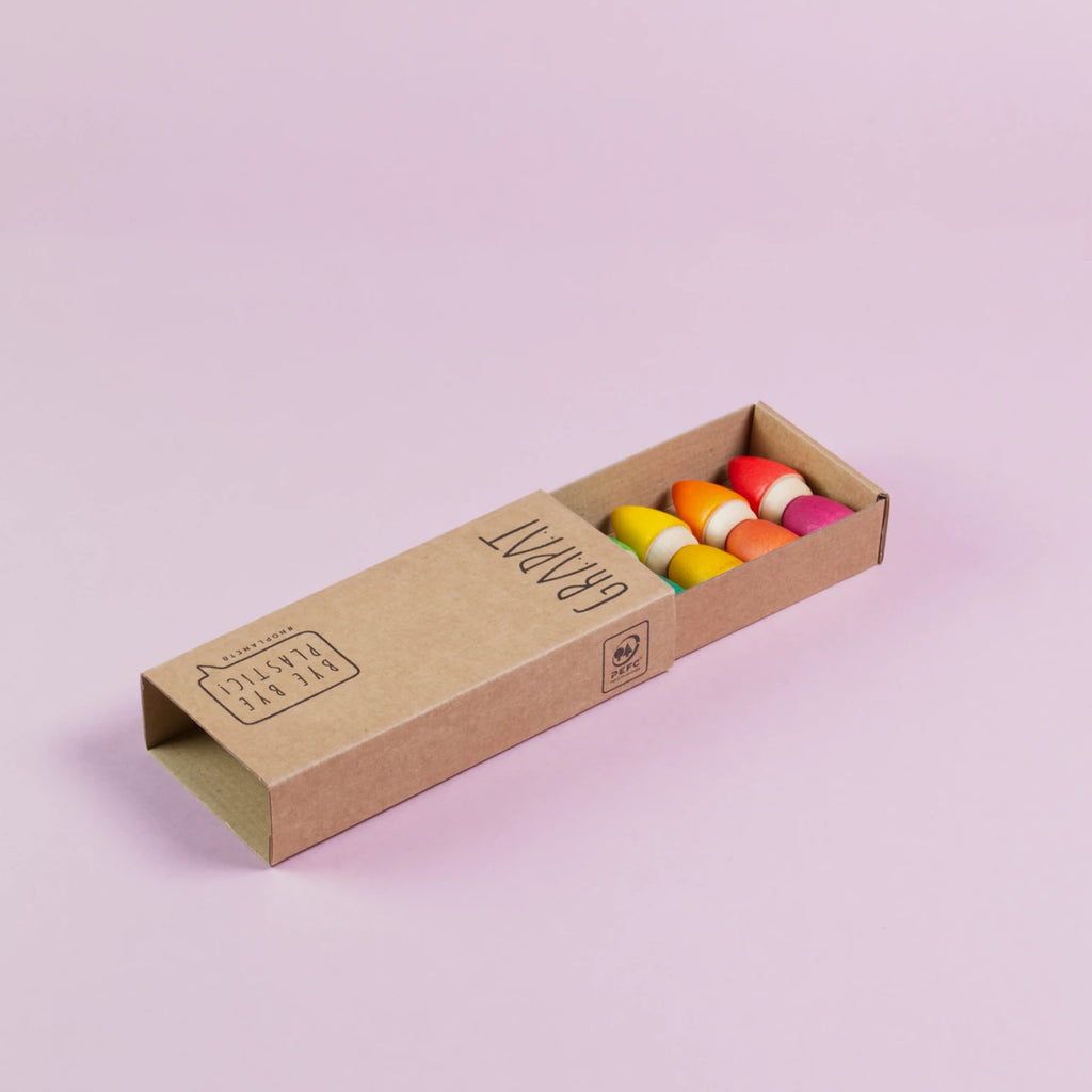 Eine halb geöffneter Produktkarton von Grapat, sind 3 von insgesamt 6 Holzfiguren von Grapat in den Farben gelb, orange und rot zu sehen.