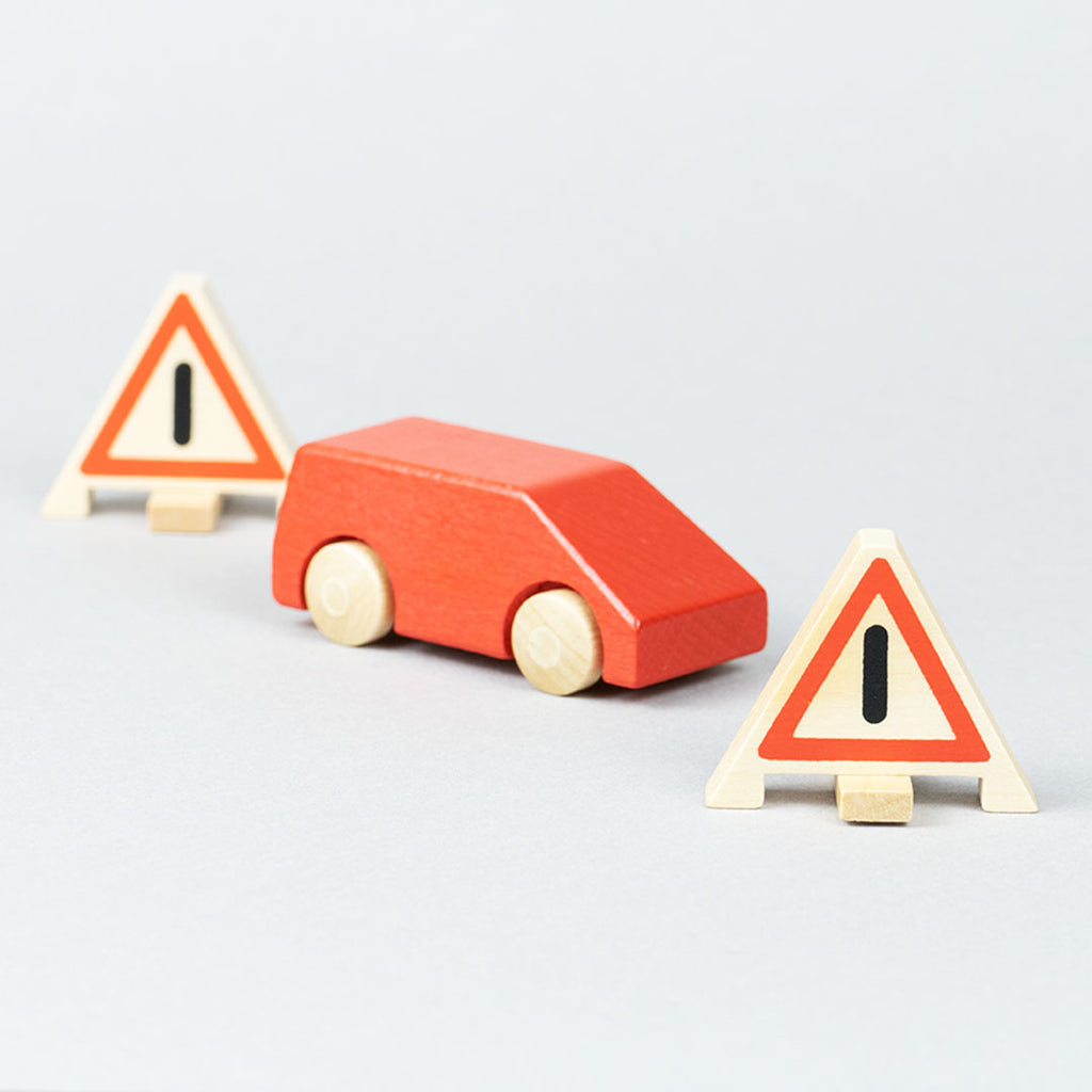 Zwei Warndreiecke aus Holz mit rotem Holzauto Typ Van dazwischen