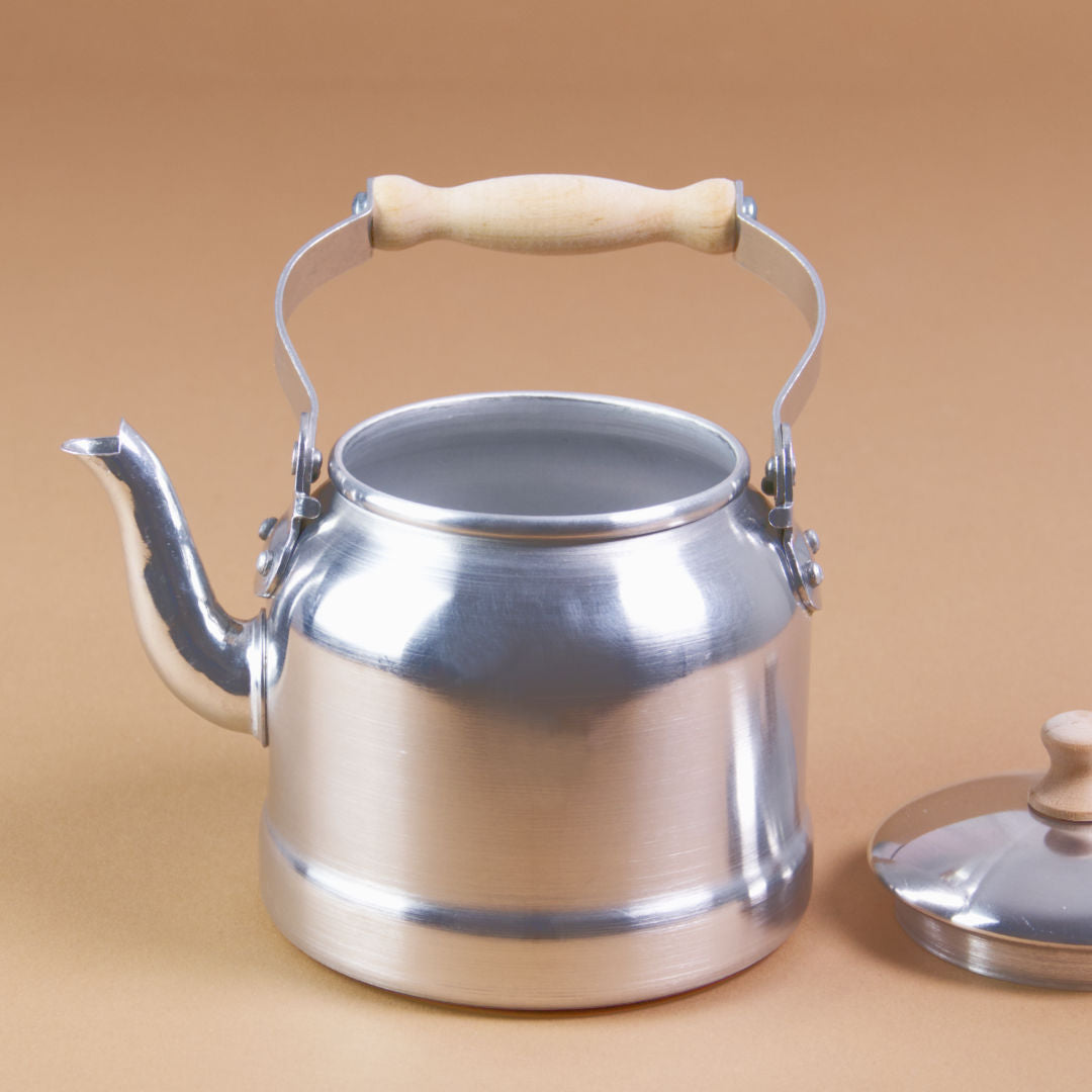 Ein Wasserkessel aus Aluminium mit bewegbarem Holzgriff und danebenliegendem Deckel.