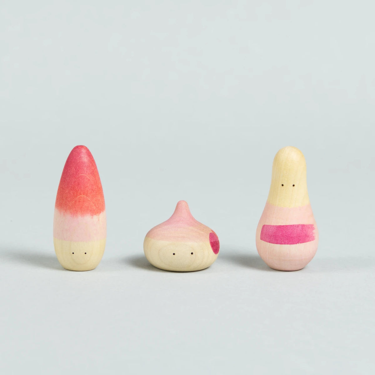 Drei organisch-geformte Holzfiguren mit Augen und rosa-roten Bemalungen.