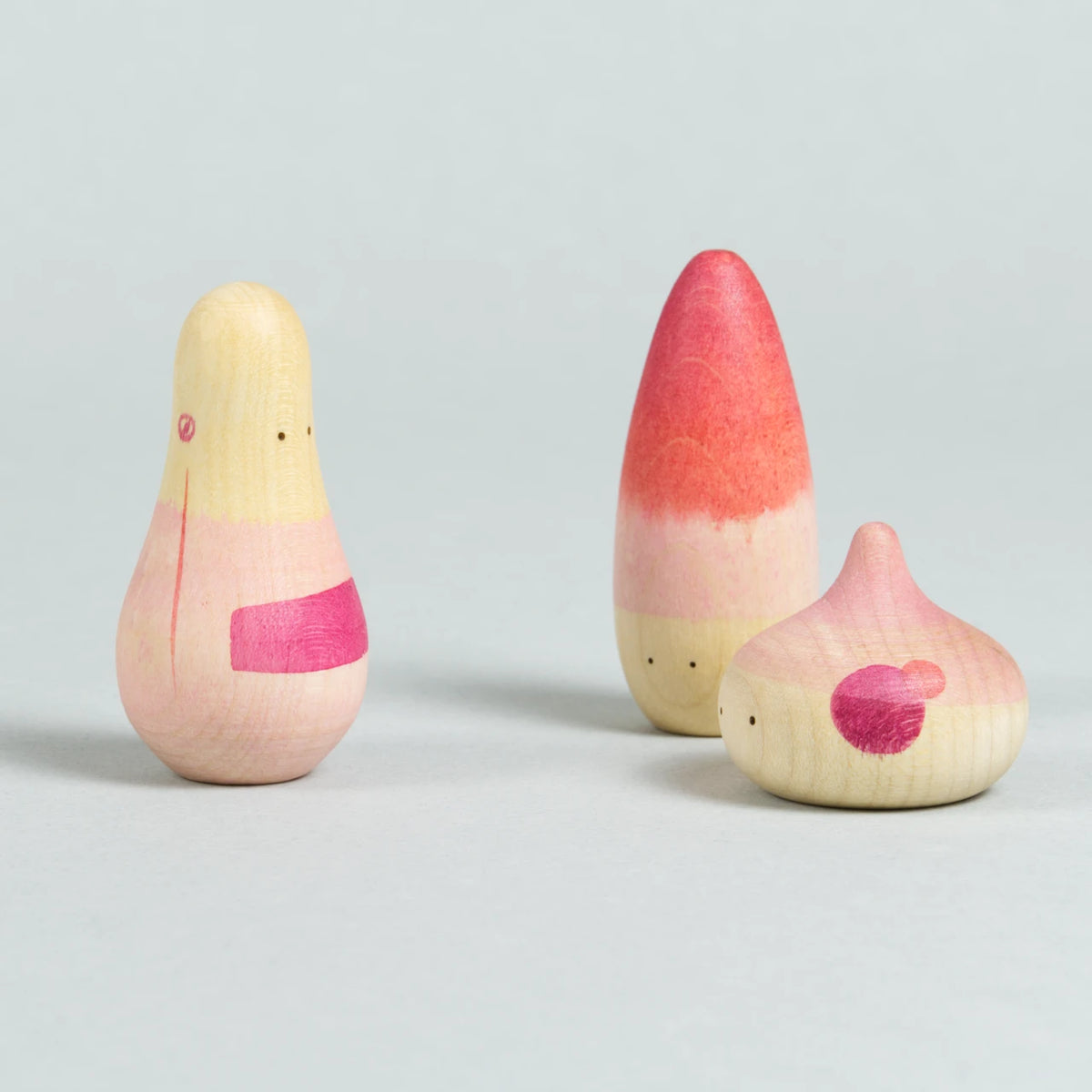 Drei organisch-geformte Holzfiguren mit Augen und rosa-roten Bemalungen.