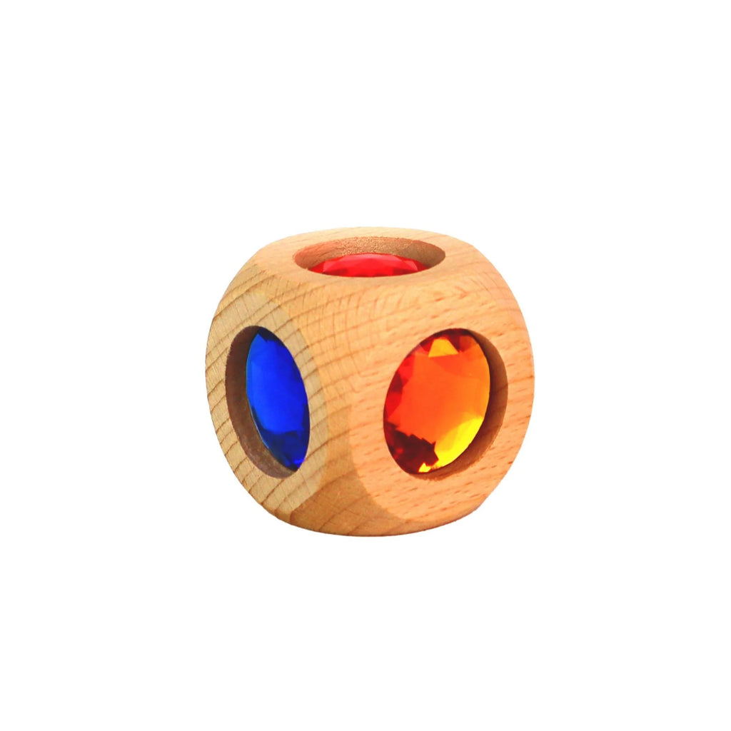 Der Zauberwürfel der Marke Bauspiel ist aus Buchenholz, die Maserung des Holzes ist hier gut zu sehen. Ausserdem sind drei der sechs Seiten sichtbar und zeigen die Acryljuwelen in den Farben Blau, Rot und Orange.