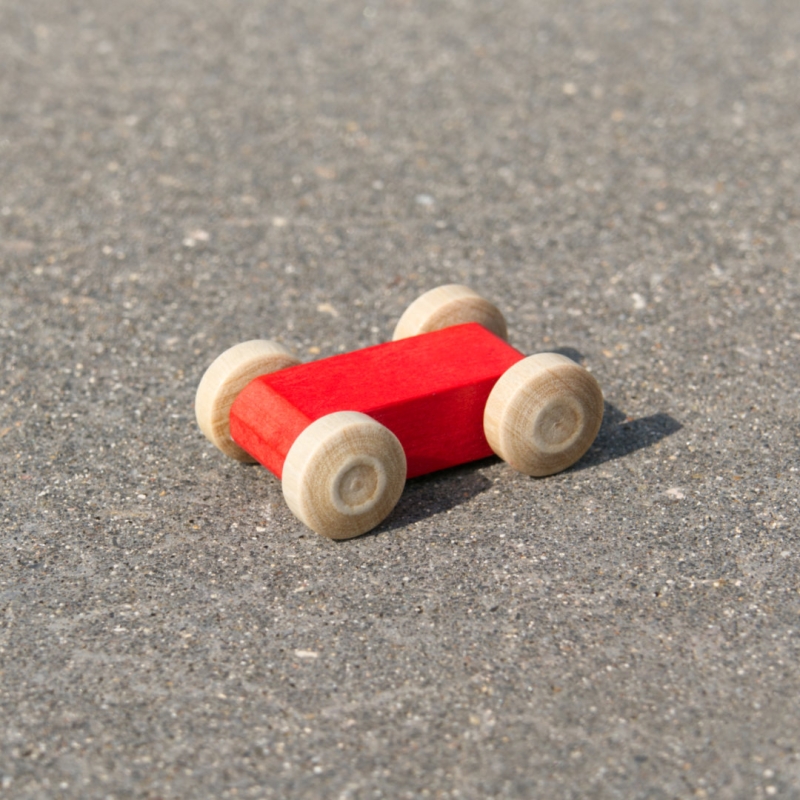 Kleines, leuchtend rotes, reduziertes Holzfahrzeug mit naturfarbenen Holzreifen, fahrbar