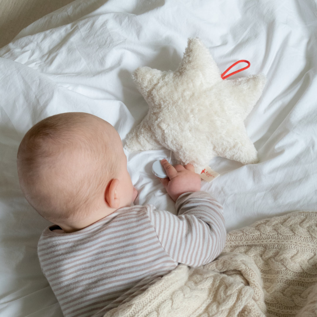 Baby spielt mit weißem Bio-Kuscheltier in Sternform, aus Schafwolle und integrierter Spieluhr