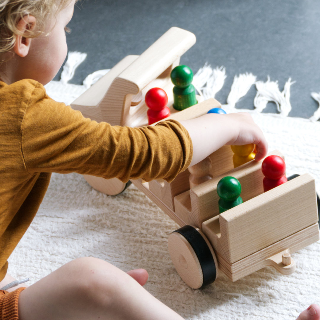 Kleinkind spielt mit Holz-Fahrzeug Typ Bus und bunten Holz-Figuren