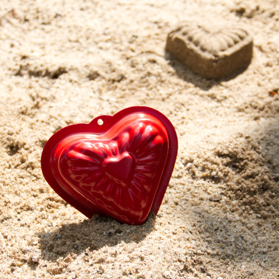 Rote Herz-Form aus Metall im Sand