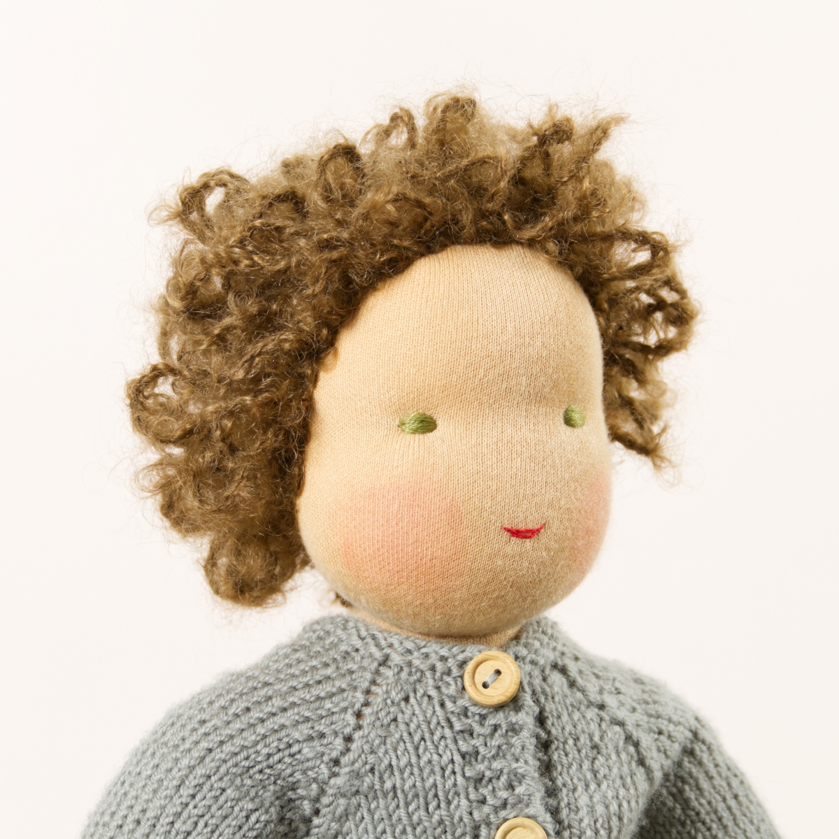 Puppe mit hellem Hautton nach Waldorf-Art, kurze braune Haare, gekleidet in grauen Strickanzug