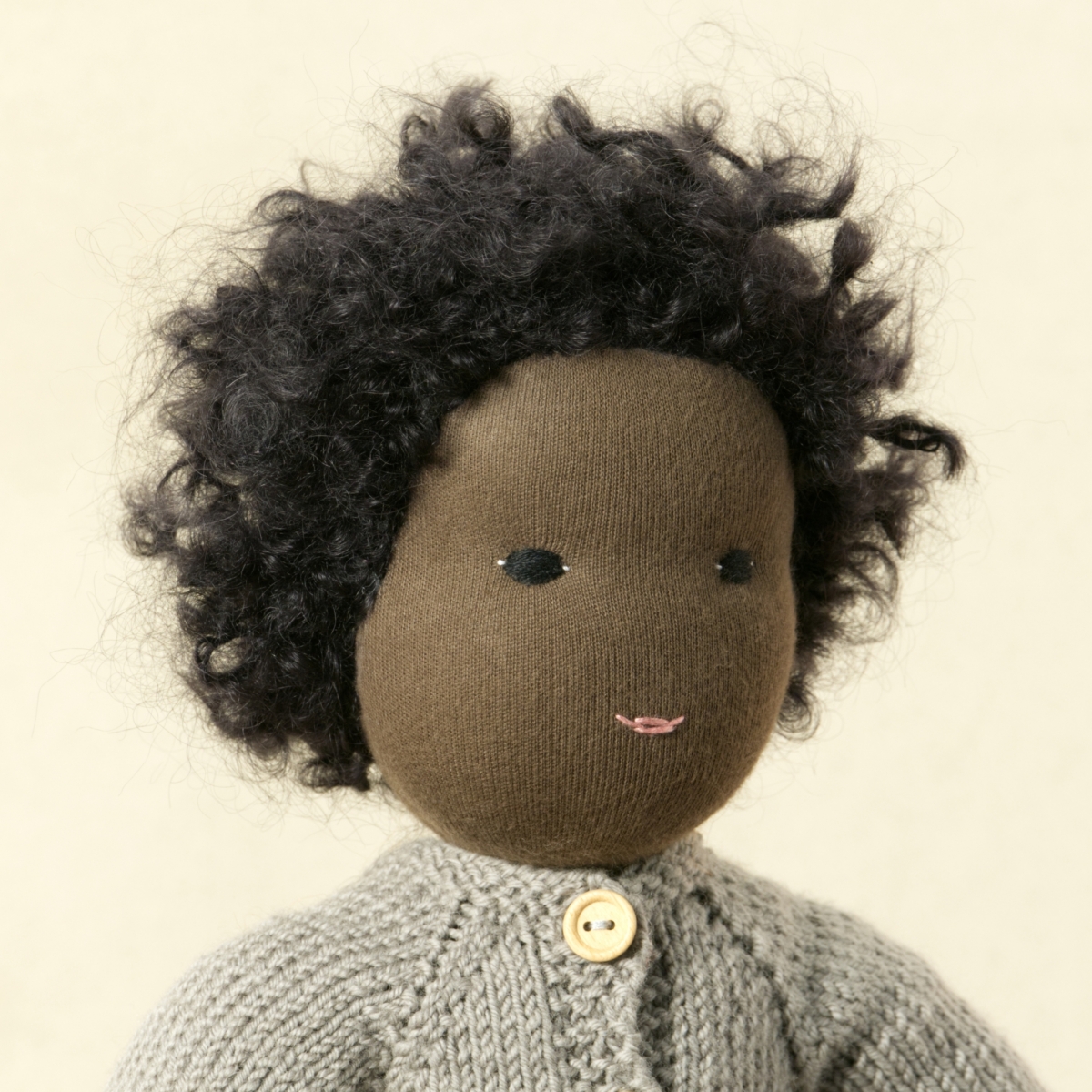 Puppe mit dunklem Hautton nach Waldorf-Art, kurze schwarze Haare, gekleidet in grauen Strickanzug