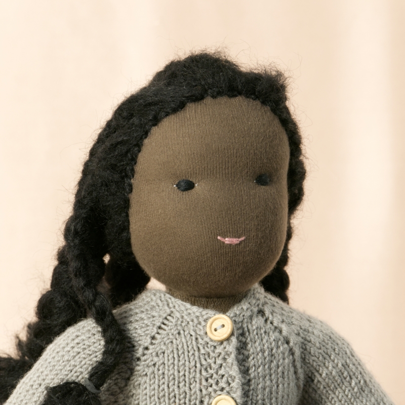 Puppe mit dunklem Hautton nach Waldorf-Art, geflochtene lange schwarze Haare, gekleidet in grauen Strickanzug