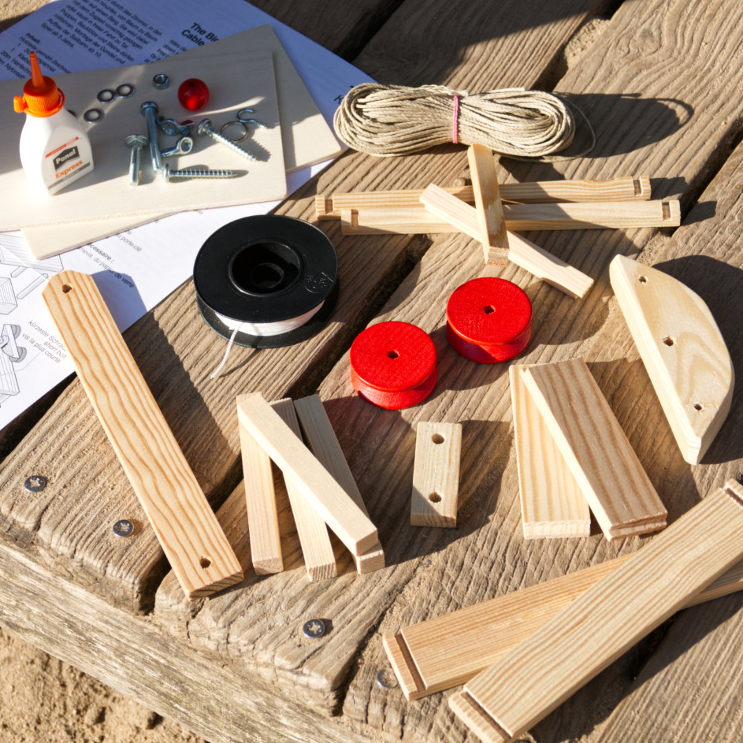 Bausatz für eine Seilbahn aus Natur-Holz mit Passagiergondel, Einzelteile ausgebreitet mit Anleitung, Schrauben und Holz-Kleber