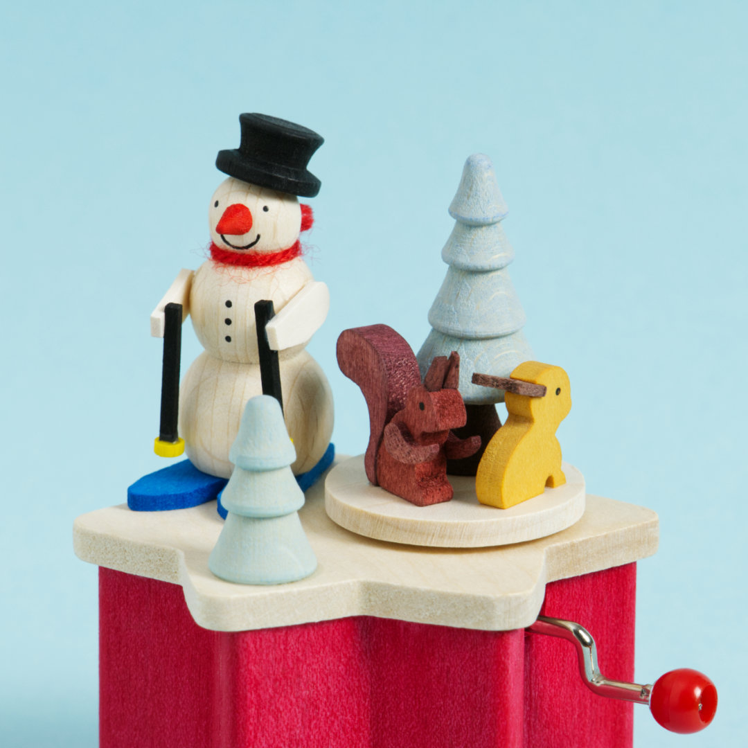 Weihnachtliche Holz-Kurbel-Spieldose in Sternform Rot, dekoriert mit einem Schneemann auf Skiern, einem braunen Eichhörnchen, einem gelben Hasen und zwei hellblauen Bäumen, Detailaufnahme Holz-Figuren