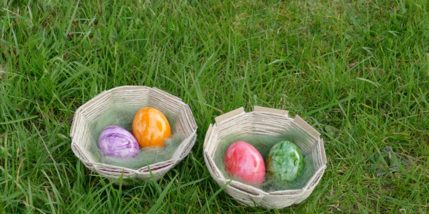 Zwei Osternestchen gefüllt mit Wolle und bunten Eiern.