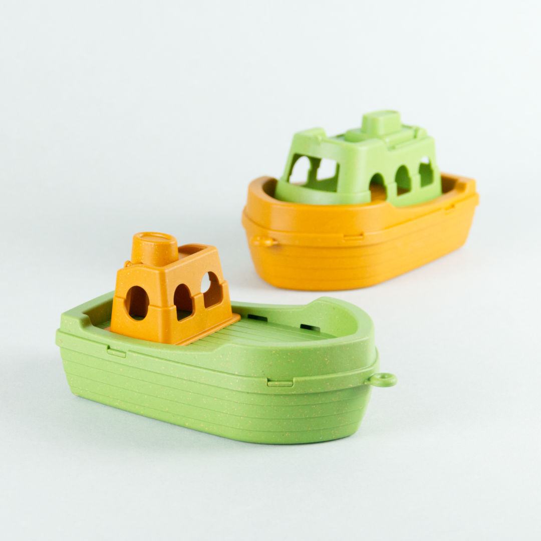 Antibakterielles Spielzeugboot, Fischkutter, Schiffsrumpf in Grün, Häuschen in Orange. Im Hintergrund die Spielzeugfähre.