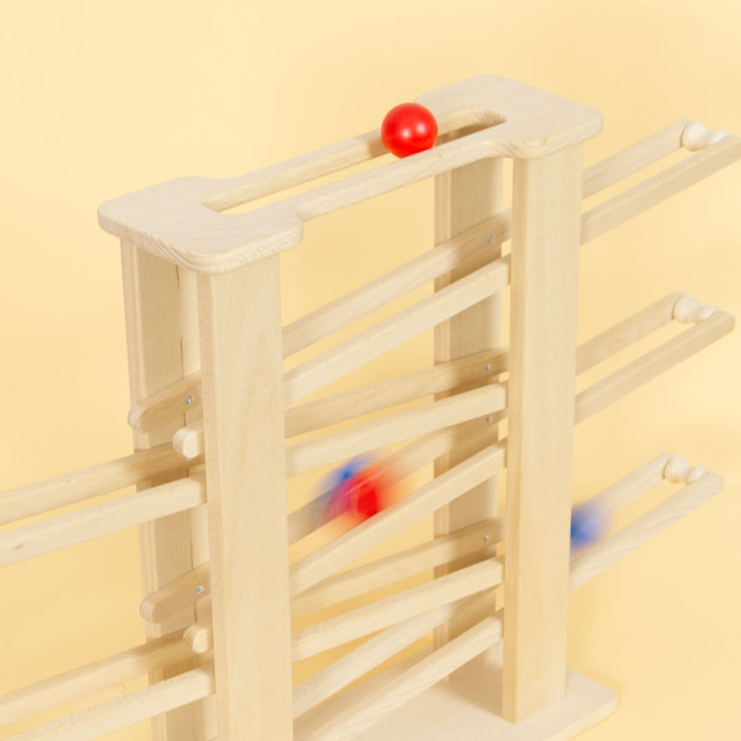 Holz Multibahn mit Zubehör, oben im Schlitz eine rote Kugl zwei weitere Objekte rollen die Bahn hinab.