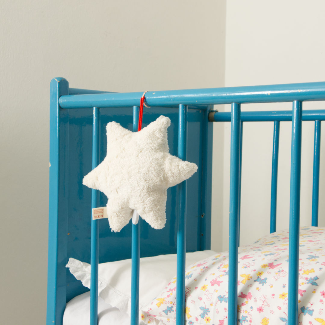 Nahaufnahme der Spieluhr in Sternenform von Kallisto in weiß, an einem blauen Kinderbett hängend.