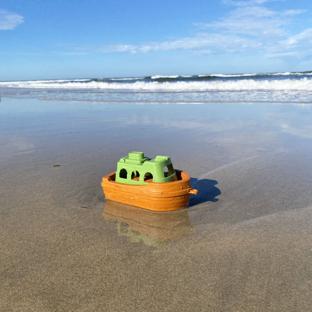 Spielzeugboot in grün und orange auf Sand am Meeresufer.