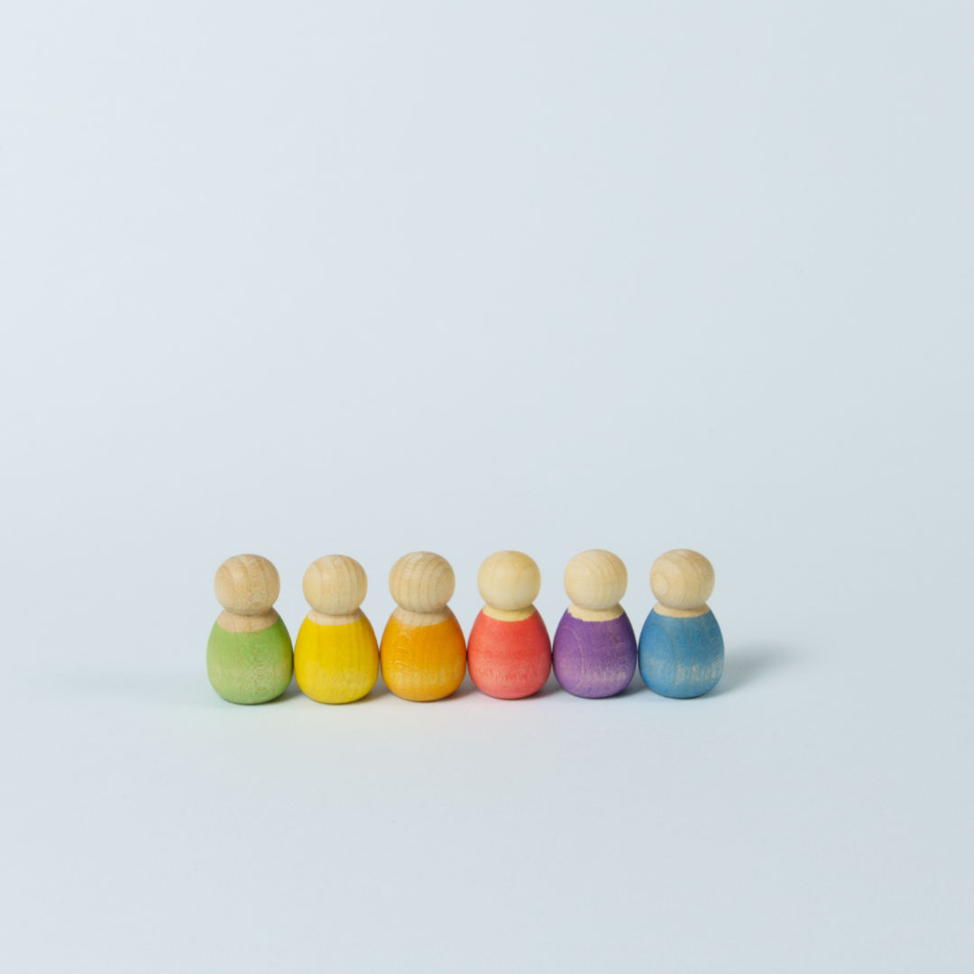 sechs kleine Babyholzfiguren in verschiedenen Farben in eine Reihe aufgestellt.