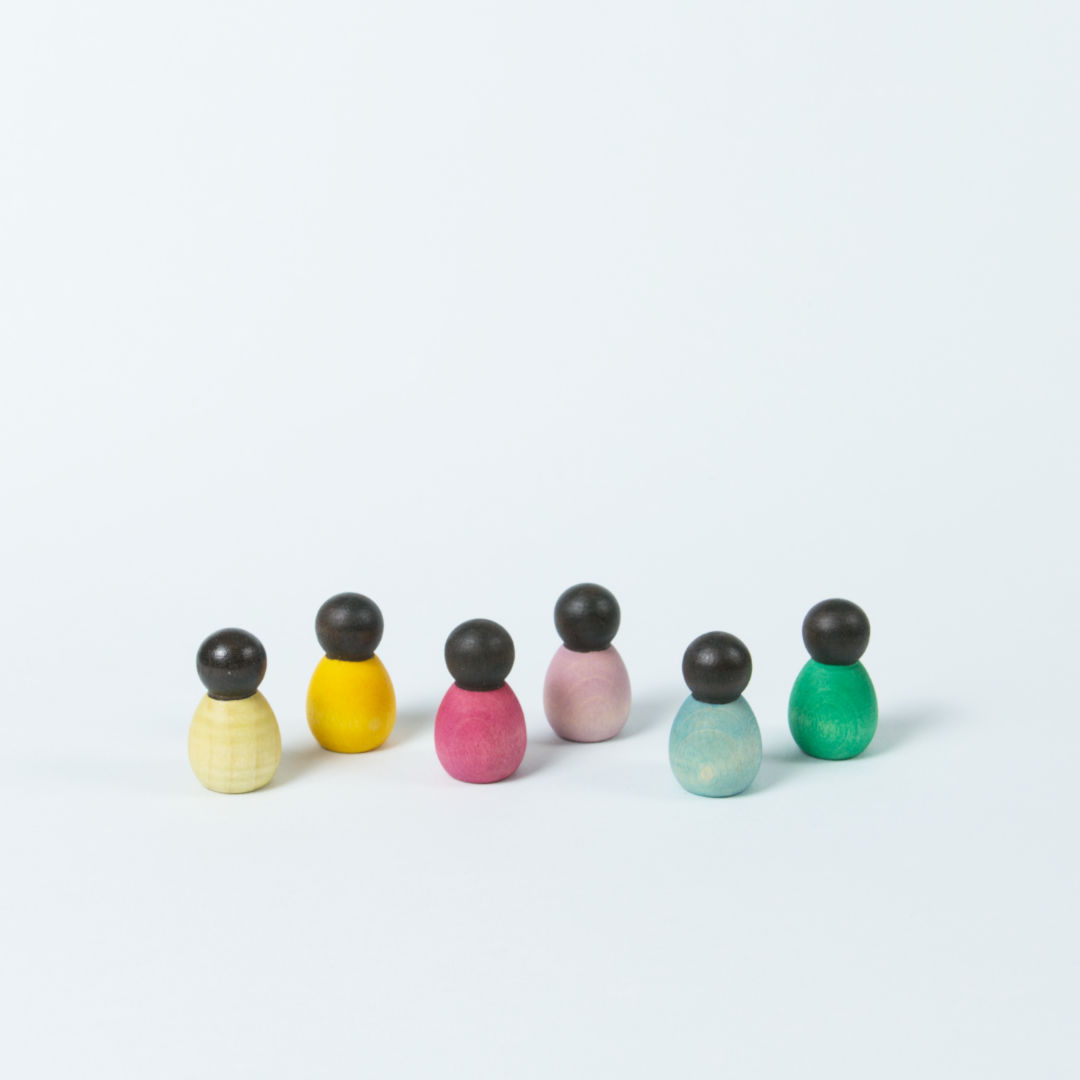 sechs kleine Babyholzfigurenmit dunkler Hautfarbe und verschiedenen Körperfarben in eine Reihe aufgestellt.