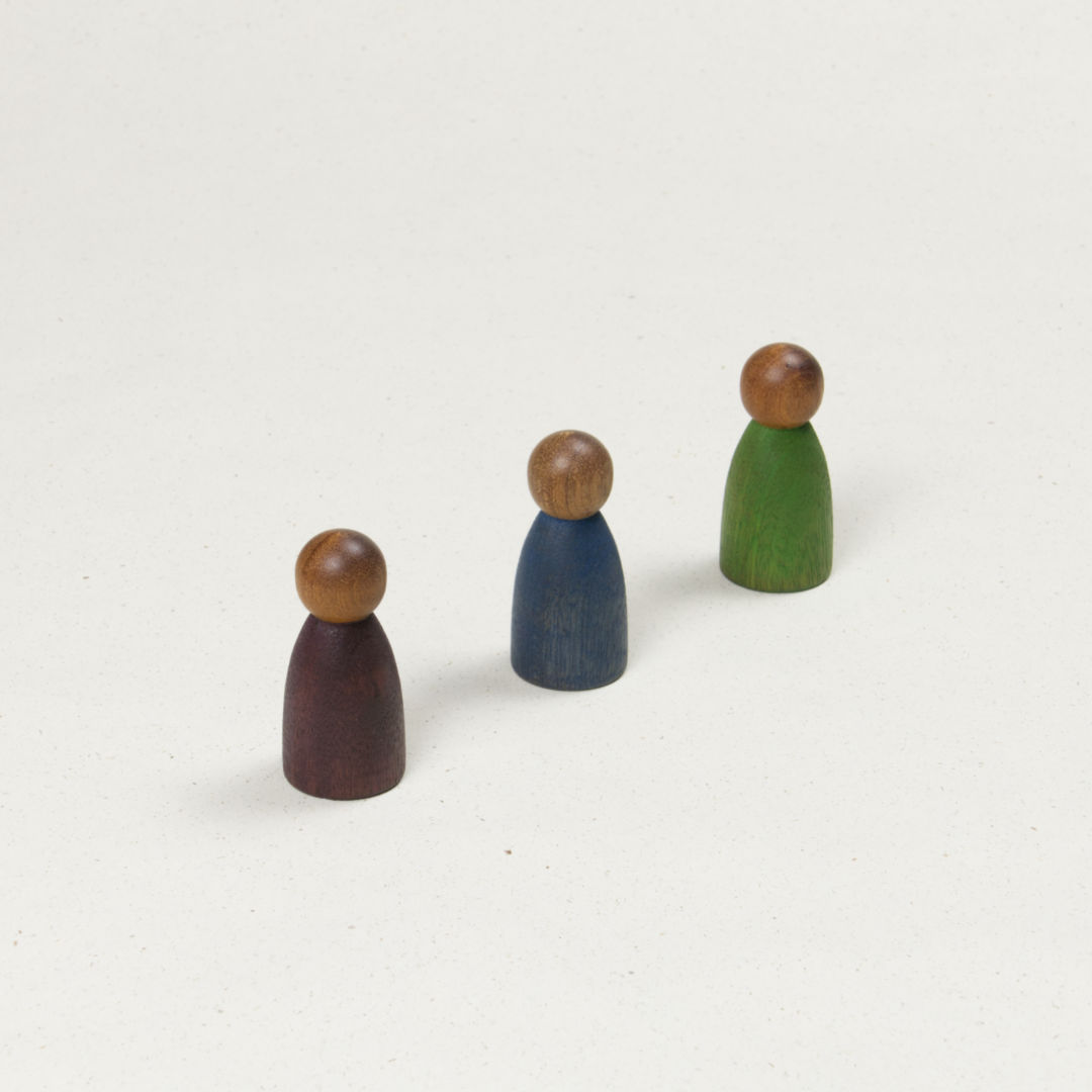 Drei gleichförmige Holzfiguren mit dunklerer Hautfarbe und Körpern in blau, lila und grün.