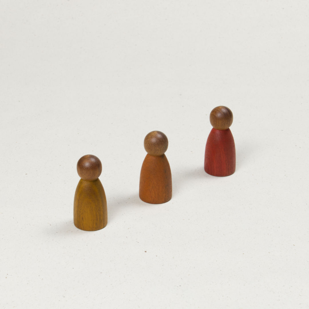 Drei gleichförmige Holzfiguren mit dunklerer Hautfarbe und Körpern in Gelb, Orange und Rot.