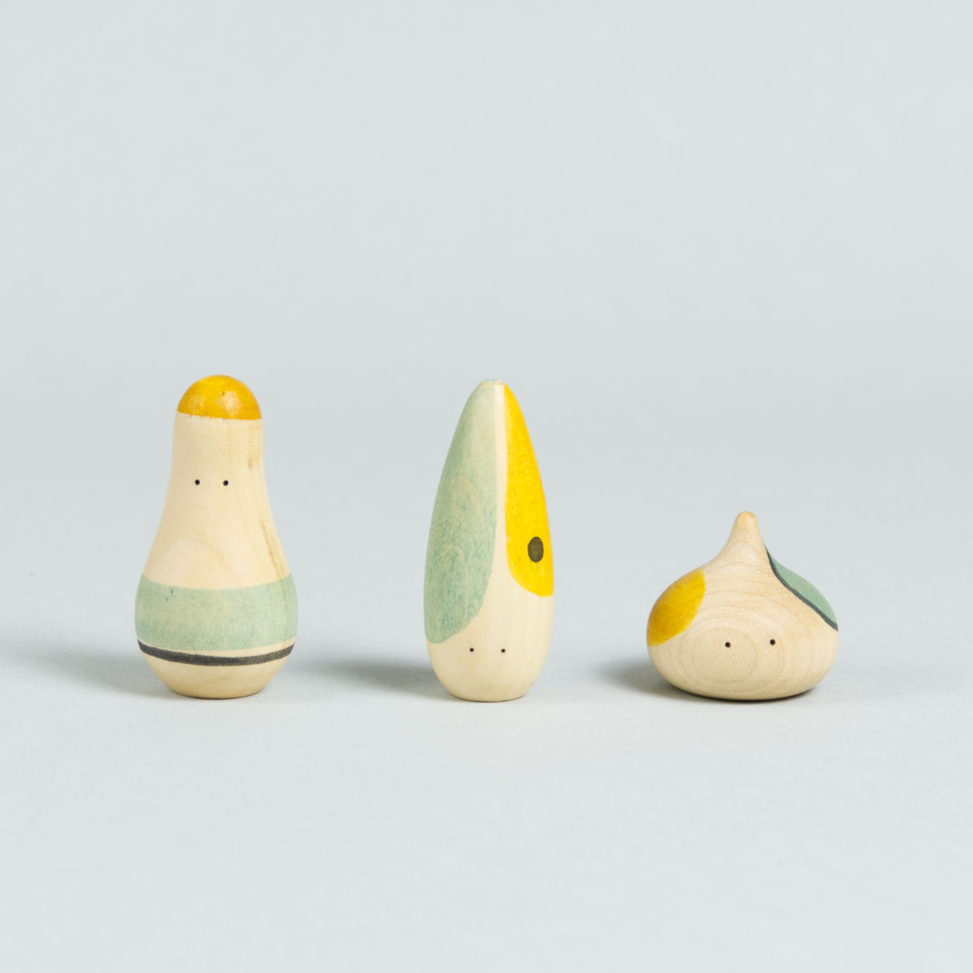 Drei organisch-geformte Holzfiguren mit Augen und türkis-gelben Bemalungen.