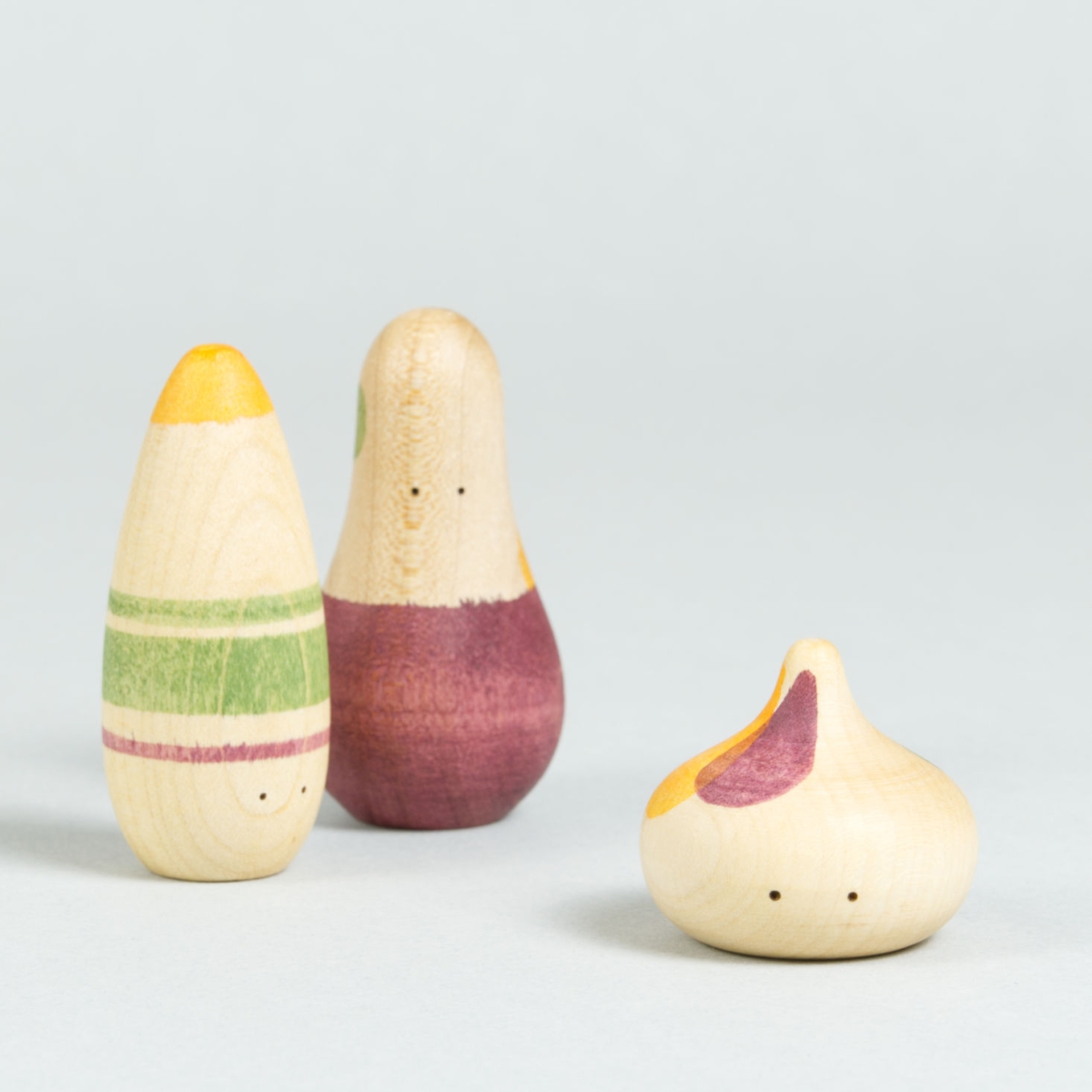 Drei organisch-geformte Holzfiguren mit Augen und weinrot, grün und orangenen Bemalungen.