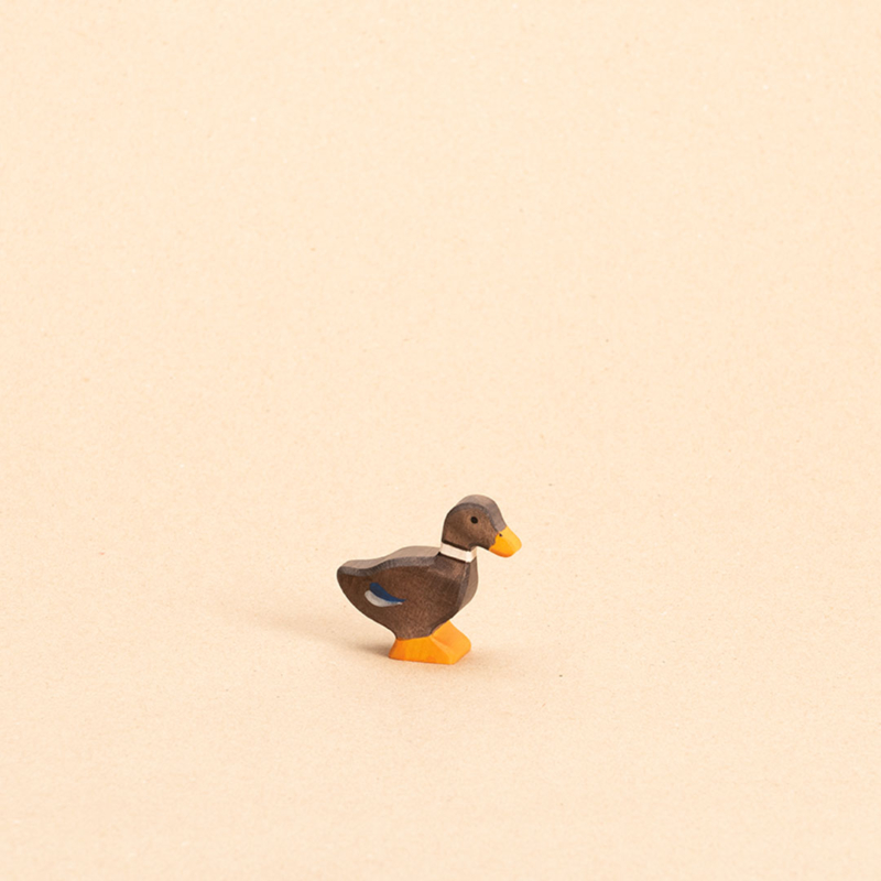 Ente aus Holz. Braun bemalt mit blauen Federakzenten und orangenem Schnabel und Entenpaddel. Nach rechts schauend