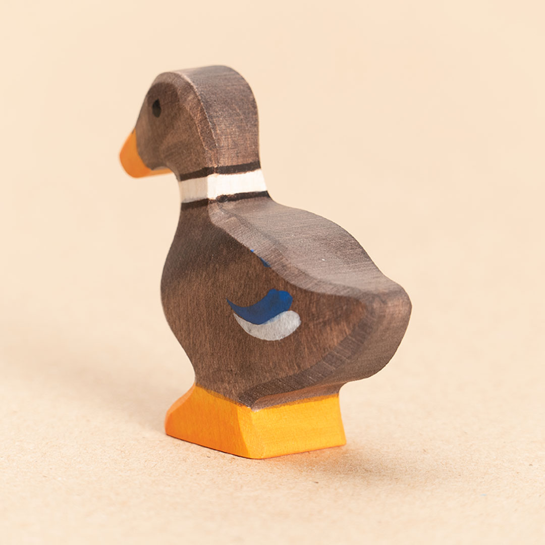Ente aus Holz. Braun bemalt mit blauen Federakzenten und orangenem Schnabel und Entenpaddel. Nach hinten links schauend