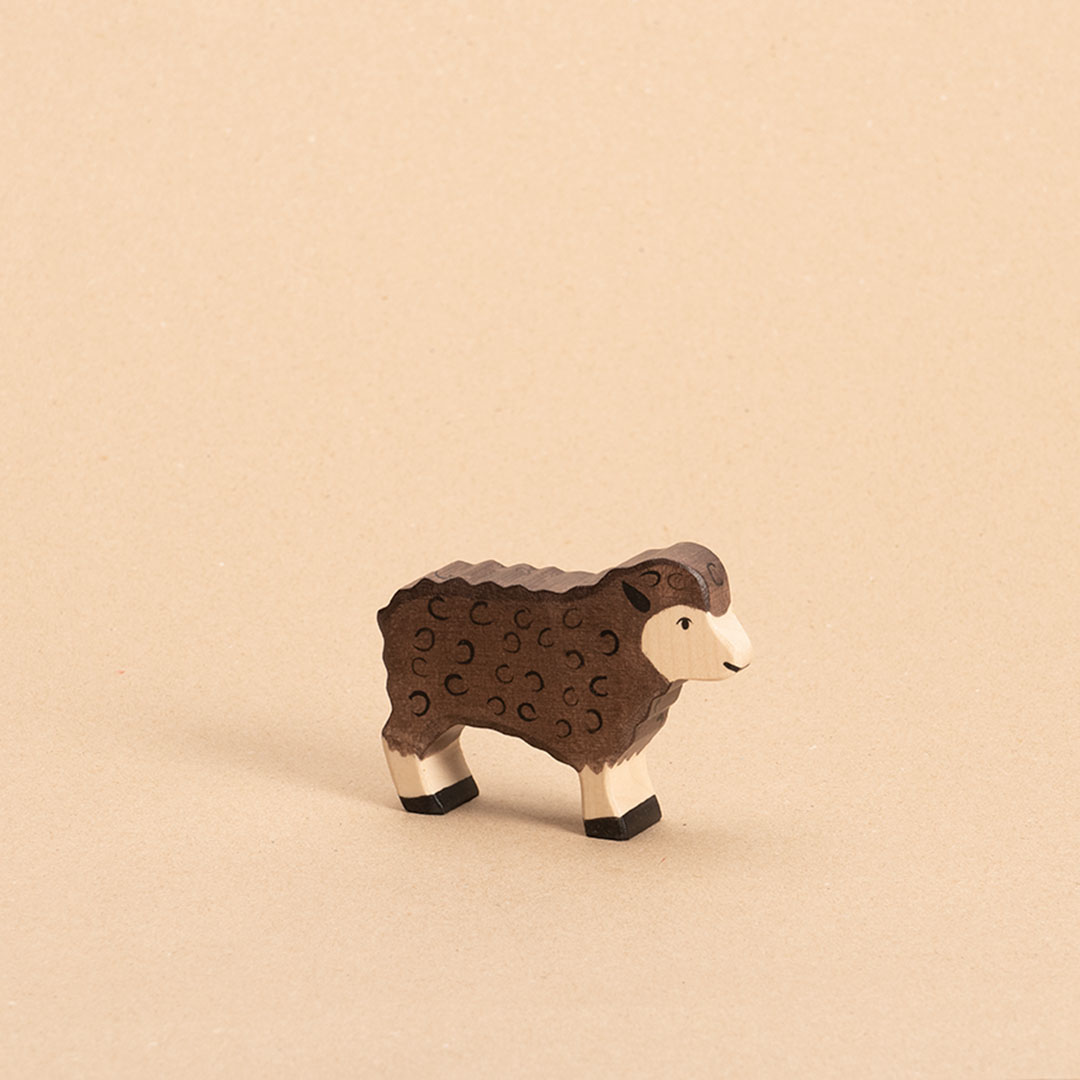 Ein dunkelbraunes Schaf aus Ahorn- und Buchenholz gefertigt, schaut im Profil nach rechts. Es hat ein naturfarbenes Gesicht, helle Beine und dunkelbraune Hufen. Das Fell wird durch schwarze, kreisförmige Bemalung deutlich.