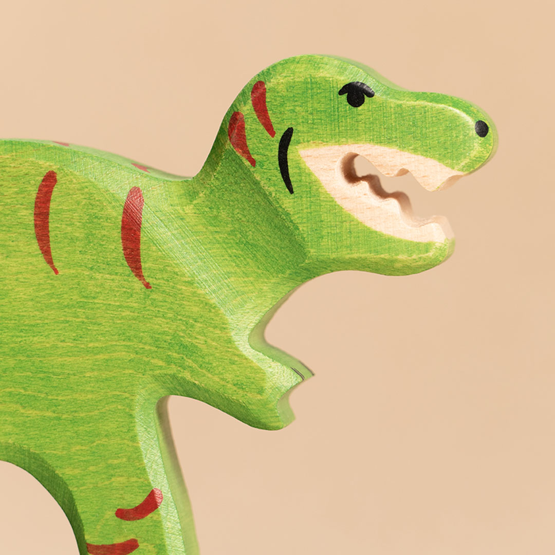 Die Nahaufnahme zeigt einen nach rechts im Profil schauenden, intensiv grünen Tyrannosaurus Rex. Sein Mund ist geöffnet und zeigt seine spitzen, weißen Zähne. Seine Haut weist rote Farbdetails auf. Er hat sehr kurze, nach vorne stehende Arme.