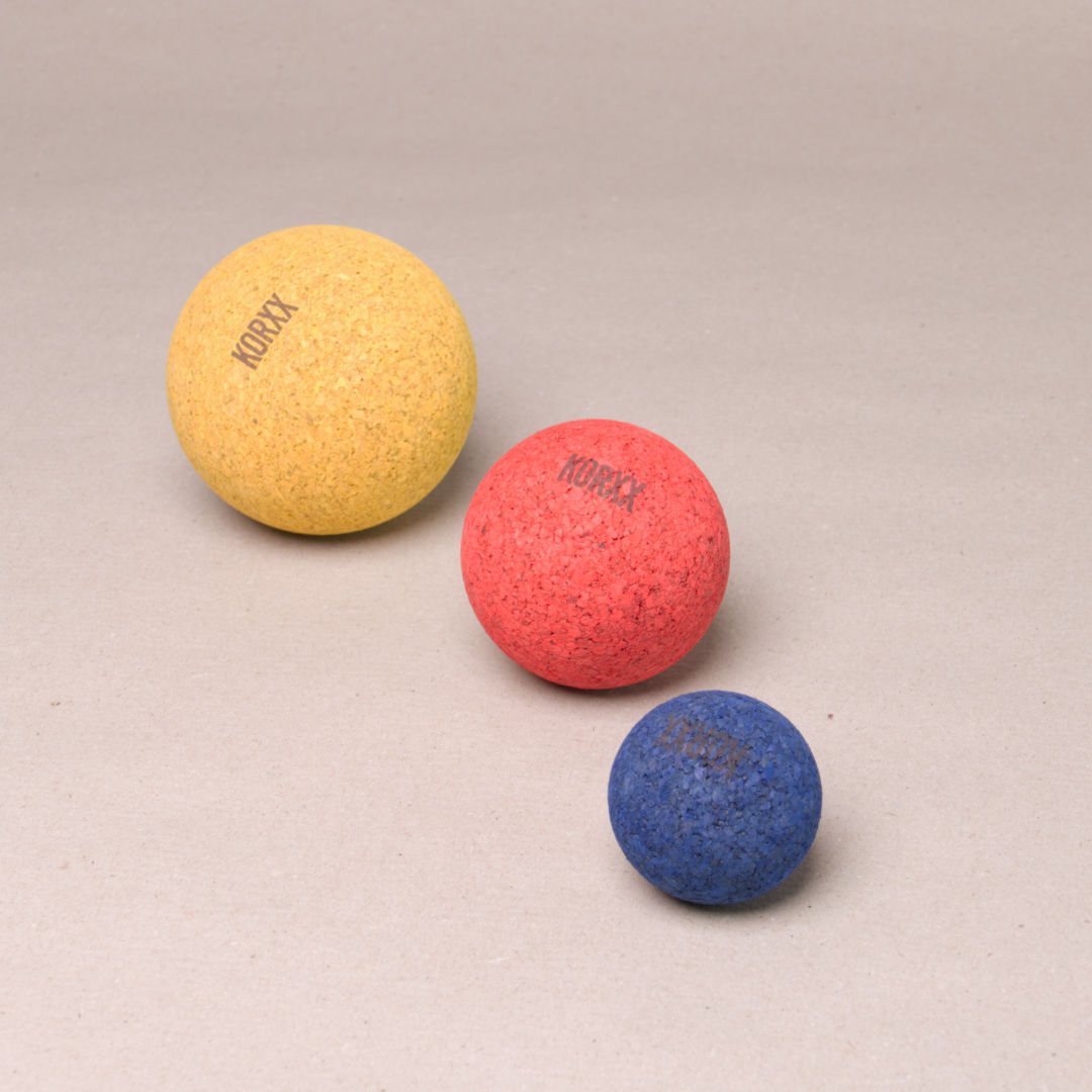 Komposition aus drei Kork Kugeln in abgestufter Größe von Korxx, die kleinste in blau, die Mittlere in rot und die Größte in gelb. Alle liegen mit dem Markenaufdruck nach oben hin da.
