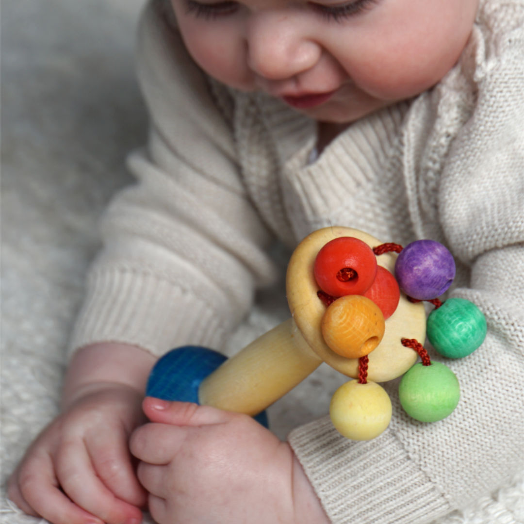 Die Holzrassel namens Karussell von Walter nic gefertigt mit bunten Perlen wird von einem Kleinkind bespielt.