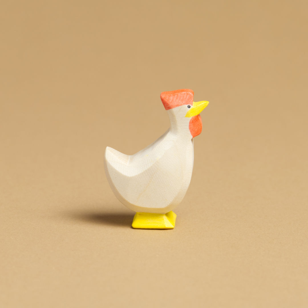 Ein weißes Huhn, das nach oben, rechts im Profil schaut, hat einen roten Kamm, einen gelben Schnabel, gelbe Füße und weisses Gefieder.